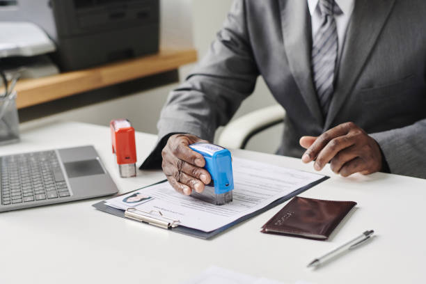 Close-up fo specialist sitting at his workplace and putting stamp on documents to approve visa